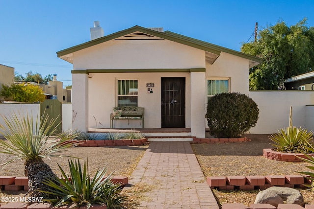 view of front of house with fence, a porch, and stucco siding