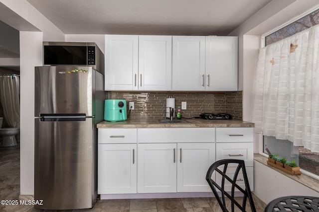 kitchen with a sink, white cabinets, light countertops, appliances with stainless steel finishes, and decorative backsplash