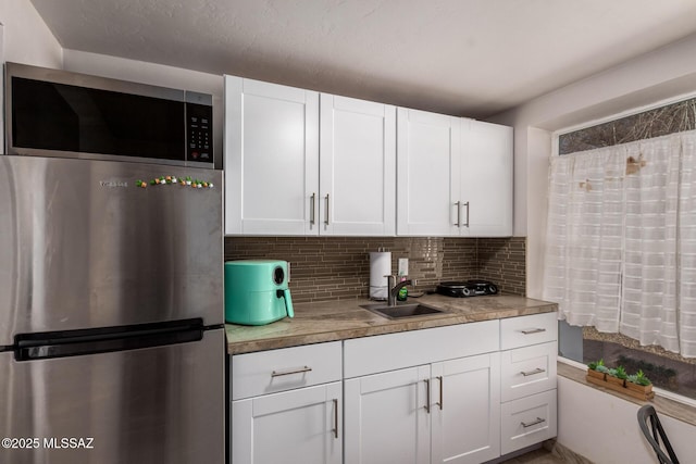 kitchen with white cabinets, a sink, stainless steel appliances, light countertops, and backsplash