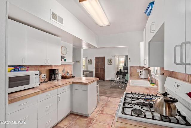 kitchen with visible vents, white cabinets, white microwave, gas range oven, and a sink