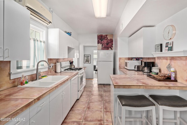 kitchen featuring decorative backsplash, white cabinets, a sink, white appliances, and a kitchen bar