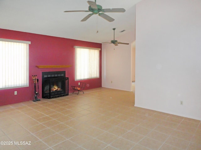 unfurnished living room with light tile patterned floors, a lit fireplace, visible vents, and a ceiling fan