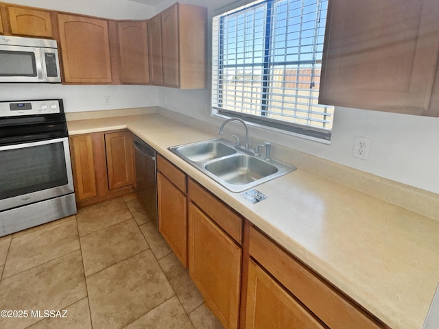 kitchen with appliances with stainless steel finishes, brown cabinets, light countertops, a sink, and light tile patterned flooring