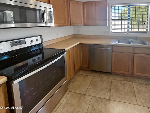 kitchen with light tile patterned floors, stainless steel appliances, a sink, light countertops, and brown cabinets