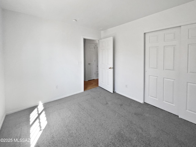 unfurnished bedroom with dark colored carpet, a closet, and baseboards