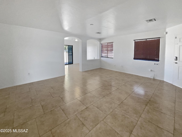 unfurnished room with arched walkways, visible vents, and light tile patterned flooring