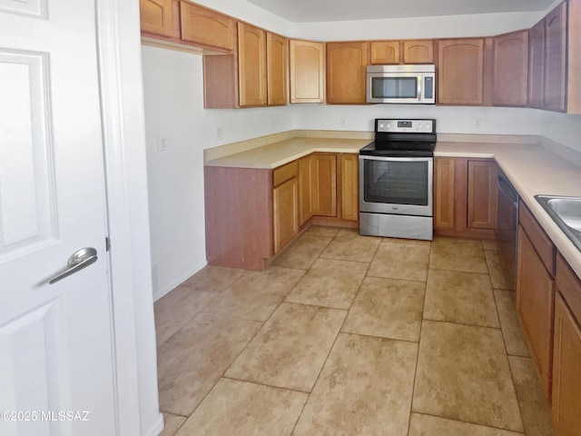 kitchen featuring stainless steel appliances, brown cabinetry, light tile patterned flooring, and light countertops