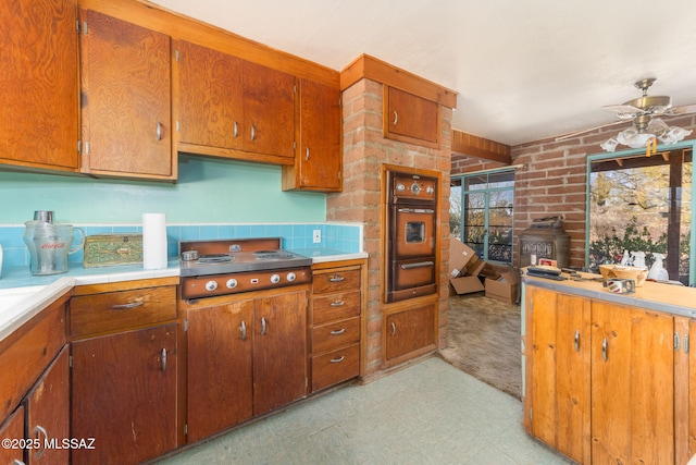 kitchen featuring cooktop, brown cabinets, oven, light countertops, and a warming drawer