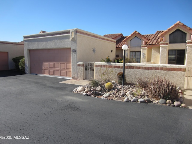 view of front of house with an attached garage, fence, driveway, a tiled roof, and stucco siding