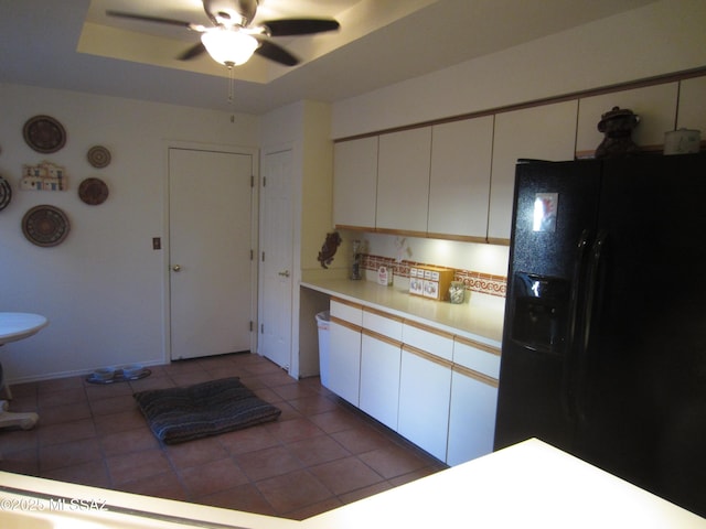 kitchen featuring tile patterned flooring, a ceiling fan, white cabinets, black fridge, and a tray ceiling