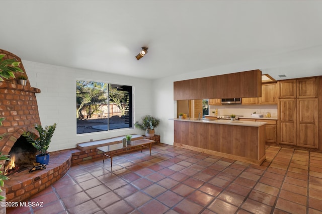 kitchen with brown cabinets, a fireplace, light countertops, stainless steel microwave, and a peninsula