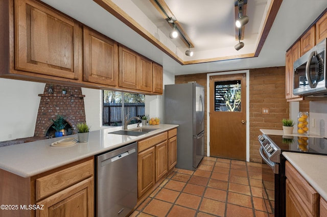 kitchen with a raised ceiling, light countertops, appliances with stainless steel finishes, brown cabinetry, and a sink