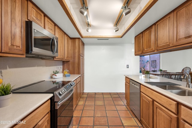 kitchen featuring stainless steel appliances, a raised ceiling, brown cabinets, and a sink