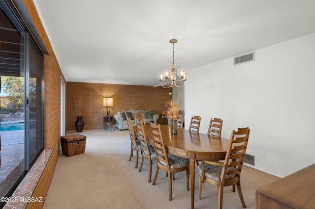 carpeted dining room featuring brick wall, visible vents, and an inviting chandelier