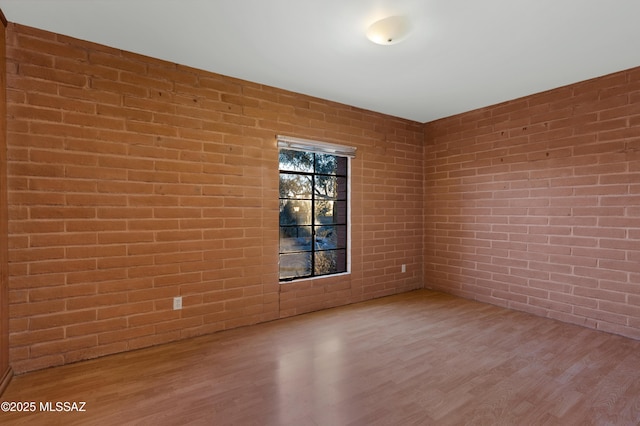 spare room with brick wall and wood finished floors