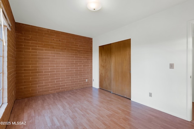 unfurnished bedroom featuring a closet, brick wall, and wood finished floors