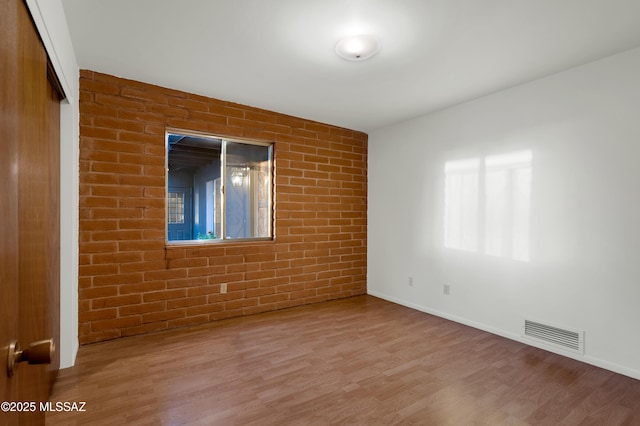 empty room featuring baseboards, brick wall, visible vents, and wood finished floors