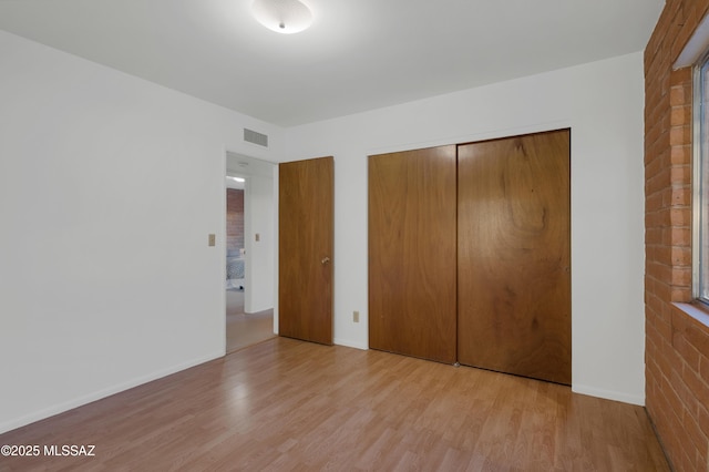 unfurnished bedroom featuring baseboards, light wood-style flooring, visible vents, and a closet