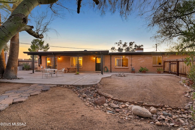 back of house at dusk featuring brick siding, a patio area, and fence