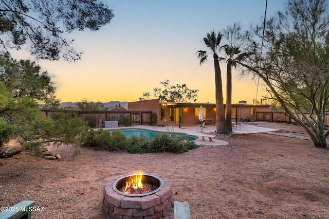 pool at dusk featuring a patio area, fence, a diving board, and a fenced in pool