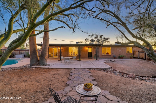 back of house at dusk with a patio, brick siding, fence, and a fenced in pool