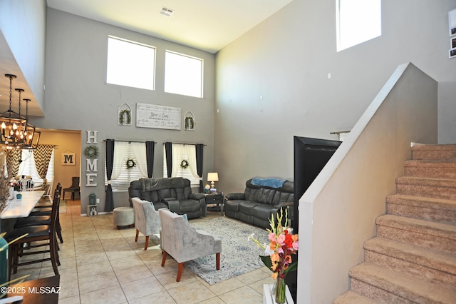 living area featuring light tile patterned floors, a towering ceiling, visible vents, stairway, and an inviting chandelier