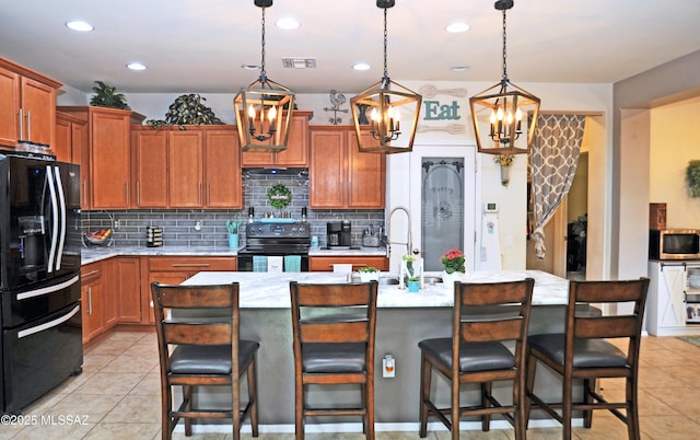 kitchen with a kitchen island with sink, a sink, visible vents, black appliances, and tasteful backsplash