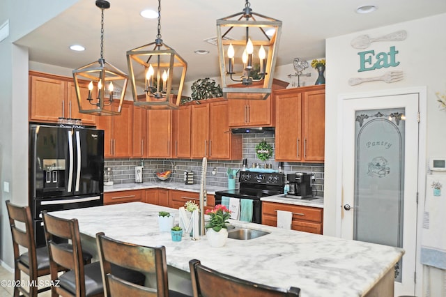 kitchen with black appliances, a breakfast bar area, a kitchen island with sink, and decorative backsplash