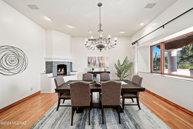 dining space with a fireplace, visible vents, an inviting chandelier, wood finished floors, and baseboards