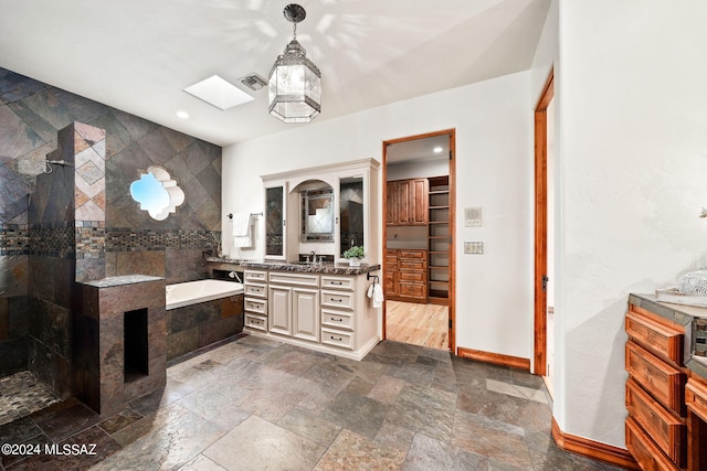 bathroom with a walk in closet, a skylight, a garden tub, visible vents, and vanity