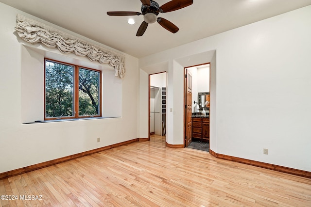 unfurnished bedroom featuring a spacious closet, light wood-style flooring, connected bathroom, ceiling fan, and baseboards