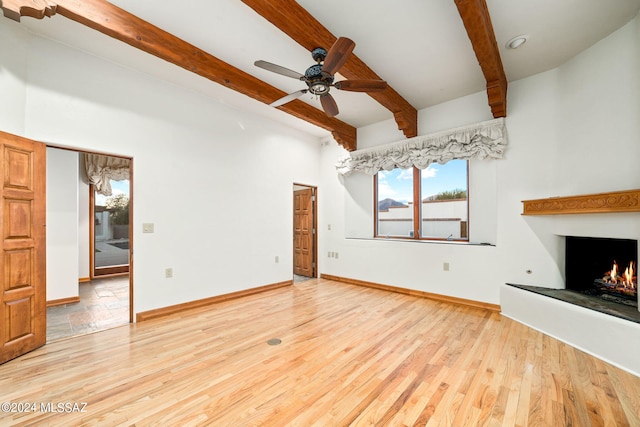 unfurnished living room with light wood-style floors, a warm lit fireplace, baseboards, and beam ceiling