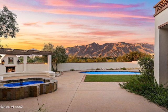 view of swimming pool featuring a patio, a mountain view, an in ground hot tub, a lit fireplace, and a fenced in pool