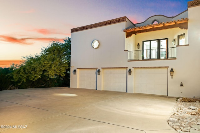 property exterior at dusk with a tile roof, driveway, a balcony, and stucco siding