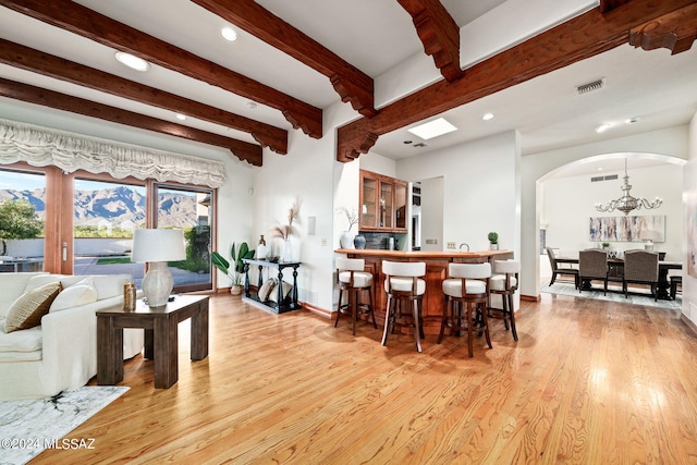 dining area with arched walkways, beam ceiling, light wood-style floors, a chandelier, and baseboards