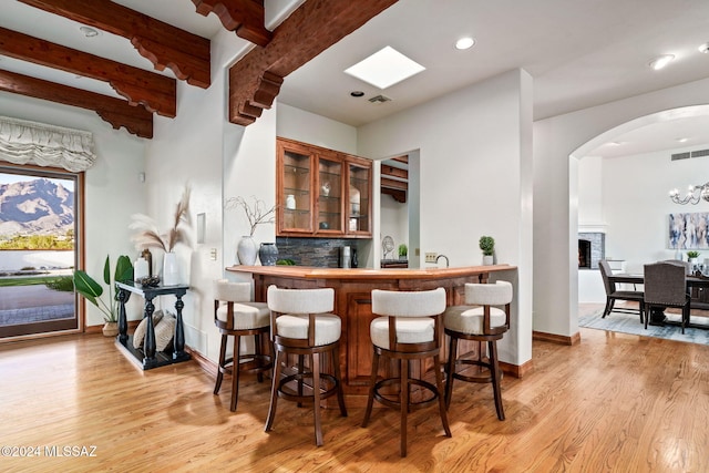 bar featuring arched walkways, visible vents, light wood finished floors, beamed ceiling, and tasteful backsplash