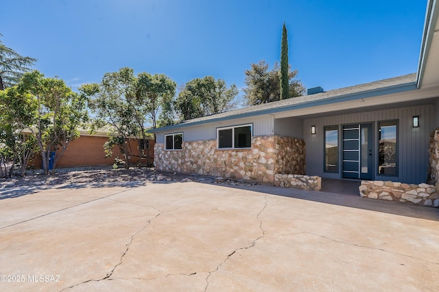 rear view of house featuring stone siding, a patio area, and fence