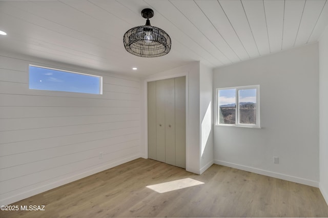 unfurnished bedroom with light wood-style flooring, multiple windows, baseboards, and a closet