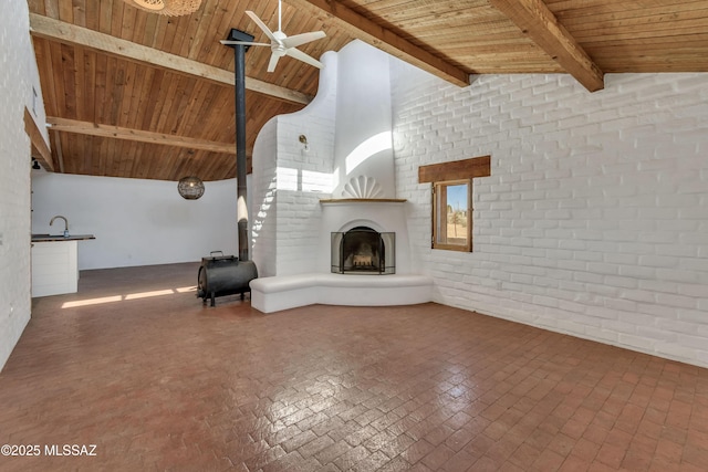 unfurnished living room featuring wooden ceiling, brick wall, a fireplace, a ceiling fan, and beam ceiling