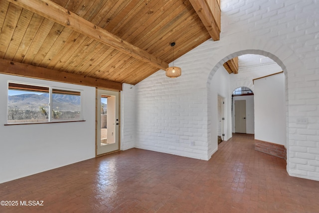 unfurnished room featuring arched walkways, wooden ceiling, brick wall, brick floor, and a mountain view