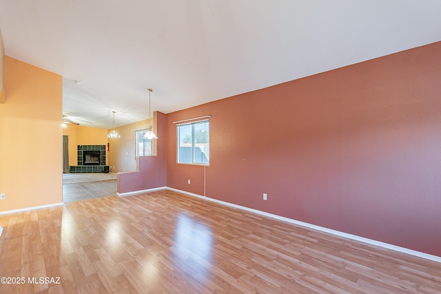 unfurnished room with light wood-style flooring, a fireplace, baseboards, and a notable chandelier