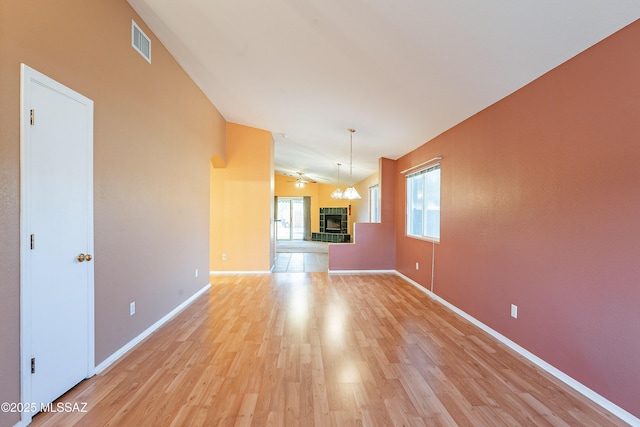 unfurnished living room with lofted ceiling, visible vents, light wood-style flooring, a tile fireplace, and baseboards