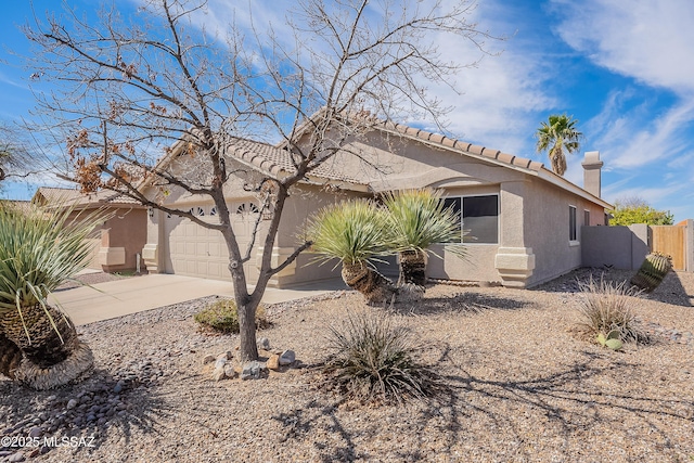 view of front of house with an attached garage, fence, driveway, stucco siding, and a chimney