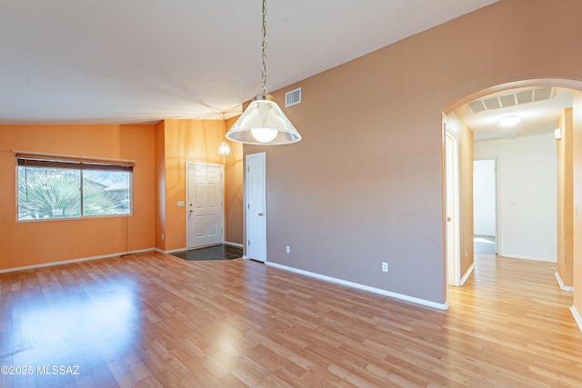 unfurnished room featuring light wood-type flooring, visible vents, arched walkways, and baseboards