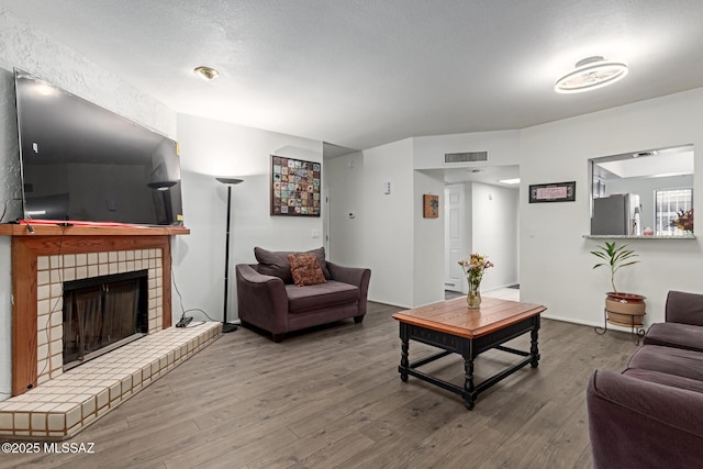 living area featuring a brick fireplace, visible vents, a textured ceiling, and wood finished floors