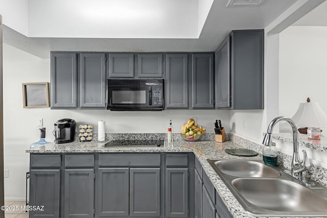 kitchen with gray cabinetry, a sink, black appliances, and light stone countertops