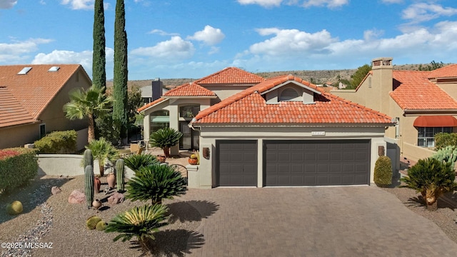 mediterranean / spanish-style house with stucco siding, a tile roof, decorative driveway, and a garage