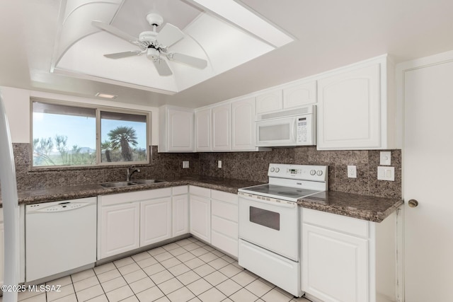 kitchen with white appliances, dark countertops, a sink, and white cabinetry