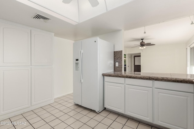 kitchen with dark countertops, white refrigerator with ice dispenser, white cabinets, and visible vents