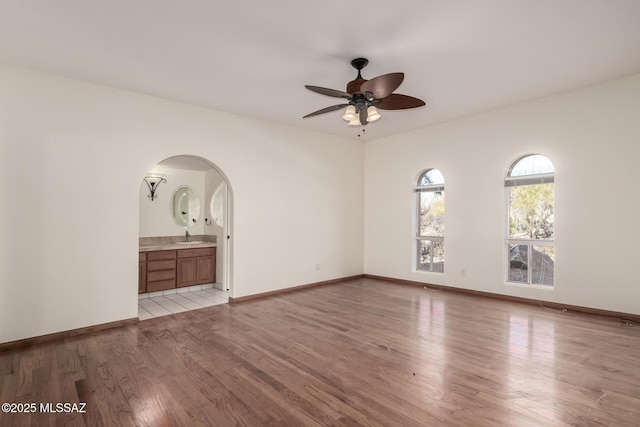 unfurnished bedroom with baseboards, arched walkways, ensuite bathroom, light wood-style floors, and a sink